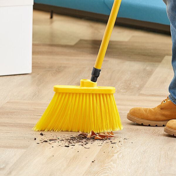 A person sweeping a wooden floor with a yellow angled broom head.