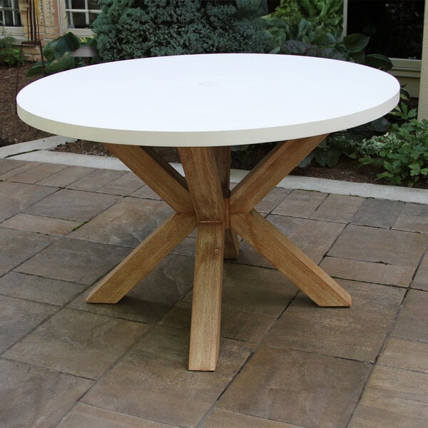 An ivory round table with a wooden top on a brick patio.