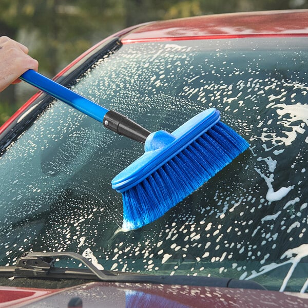 A hand with a blue Lavex Flo-Thru scrub brush cleaning a car window.