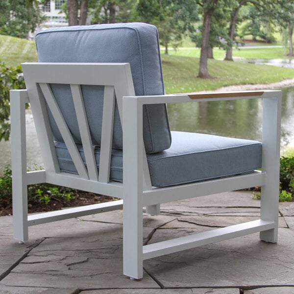 An Outdoor Interiors white aluminum arm chair with blue cushions on a stone patio.
