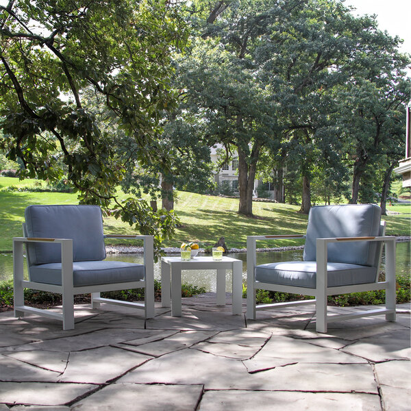 A white Outdoor Interiors arm chair with blue cushions on a stone patio table.