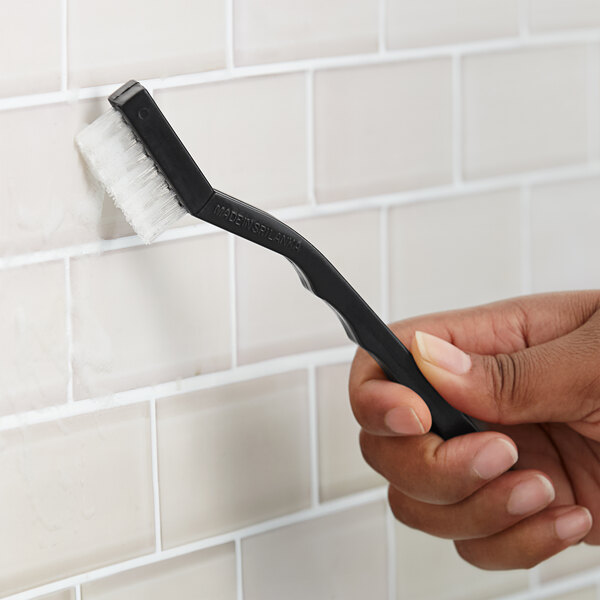 A toothbrush-style grout brush with unflagged nylon bristles being used to clean tile grout.