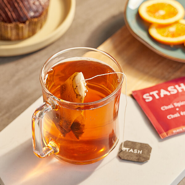 A glass mug of Stash Chai Spice tea with a tea bag in it on a table.