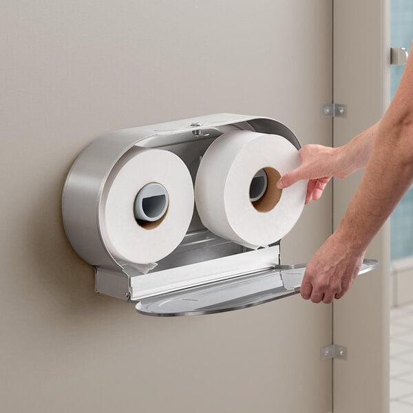 A man's hand reaching for toilet paper in a Lavex stainless steel double-roll toilet paper dispenser.