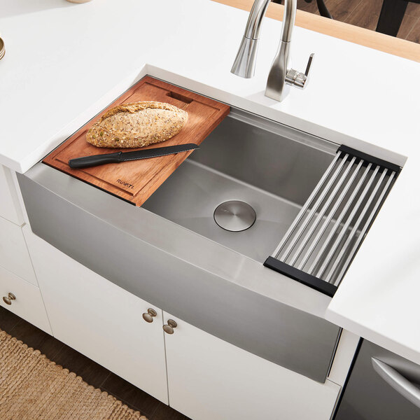 A Ruvati stainless steel farmhouse sink with a wooden cutting board over the basin.