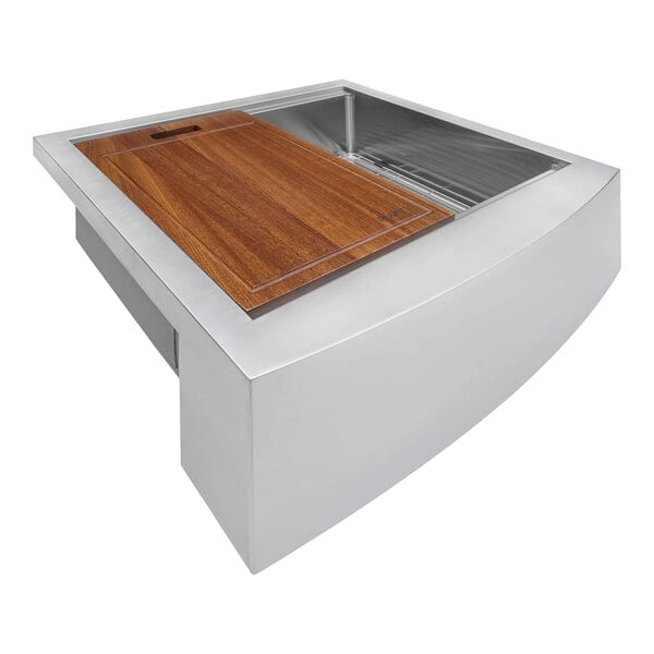 A Ruvati stainless steel farmhouse sink with a wooden cutting board over it.