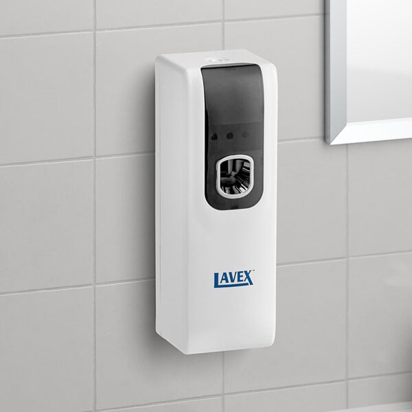 A Lavex white metered aerosol air freshener system on a tile wall.