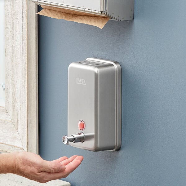 A hand using a Lavex stainless steel surface mounted liquid soap dispenser.