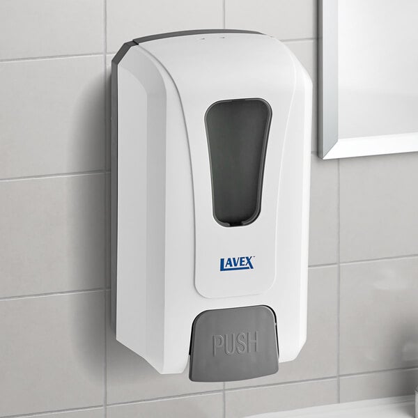 A white and gray Lavex manual foaming soap dispenser on a tile wall.