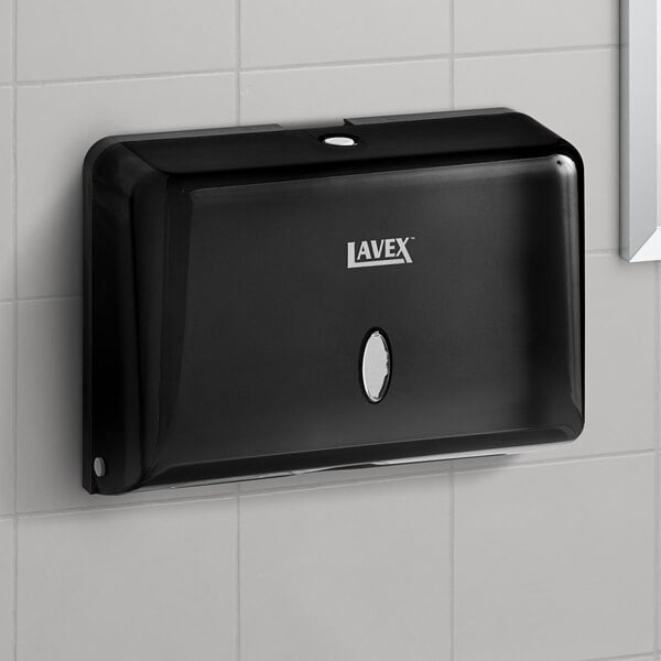 A black rectangular Lavex Mini Paper Towel Dispenser on a white tile wall.