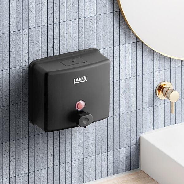 A black Lavex stainless steel manual liquid soap dispenser on a tile wall.