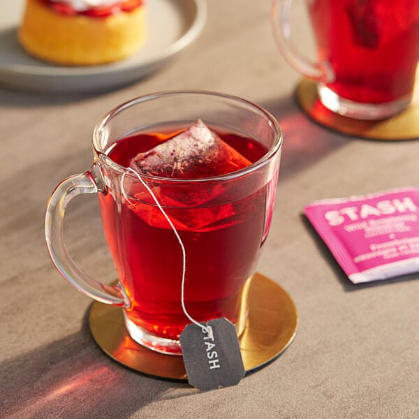 A glass mug of red Stash Wild Raspberry Hibiscus tea with a tea bag on a gold plate.