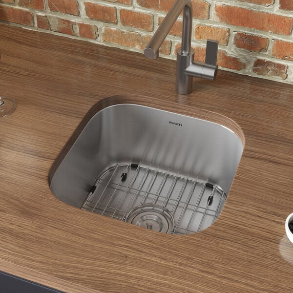 A Ruvati stainless steel undermount sink with a drain, a wine glass, and a cup of coffee.