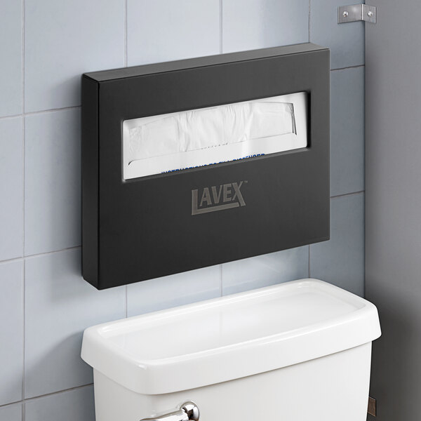 A black Lavex toilet seat cover dispenser on a wall above a toilet.