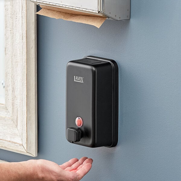 A person using a Lavex Matte Black wall mounted liquid soap dispenser.