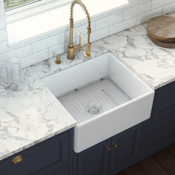 A white Ruvati Fiamma farmhouse sink with a gold faucet over a marble countertop.