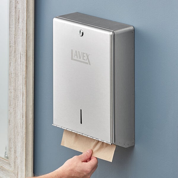 A man with a beard putting a paper towel in a Lavex stainless steel paper towel dispenser on a wall.