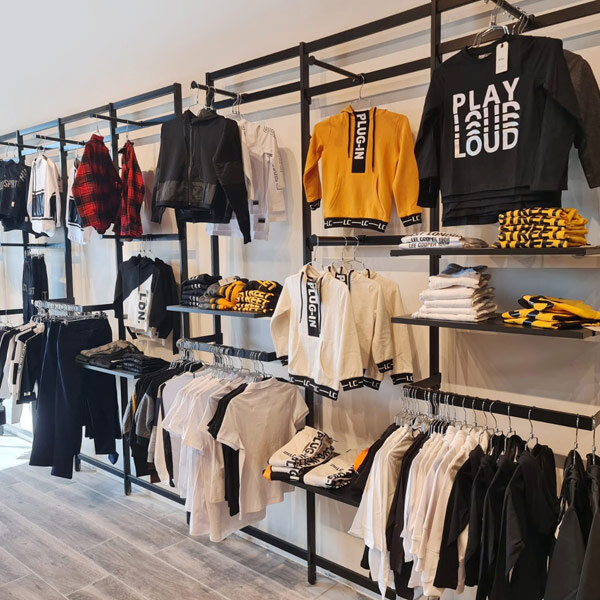 A black UDIZINE wall-mount retail clothing display with clothes hanging on faceouts and hanging rails.