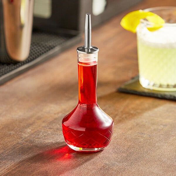 An Acopa glass bitters bottle filled with red liquid on a table.