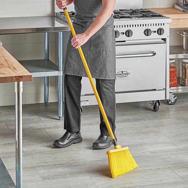 A person in an apron sweeping a floor with a yellow Lavex angled broom.