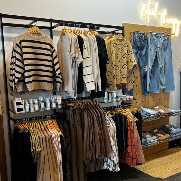 A black UDIZINE wall-mount clothing display with faceouts and hanging rails holding clothes on shelves.