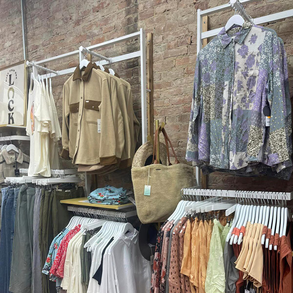 A UDIZINE white wall-mount clothing display with faceouts and hanging rails holding white shirts.