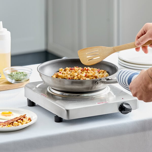 A single burner stainless steel portable electric hot plate with a cast iron element being used to cook food in a frying pan.