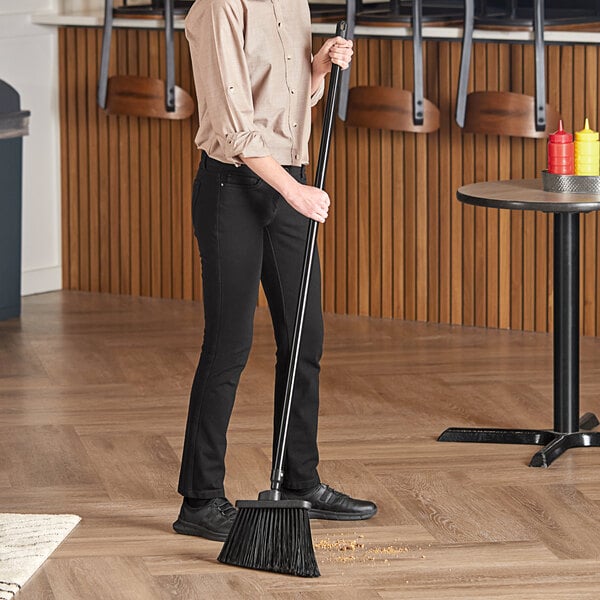 A woman sweeping the floor with a Lavex angled broom with a black metal pole.