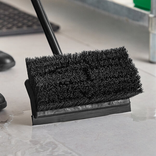 A black Lavex brush head with a squeegee being used to clean a floor.