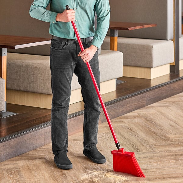 A man using a Lavex red broom with a metal handle to sweep the floor in a restaurant.