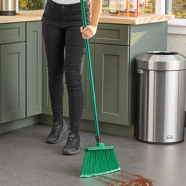 A woman sweeping a floor with a green Lavex broom.