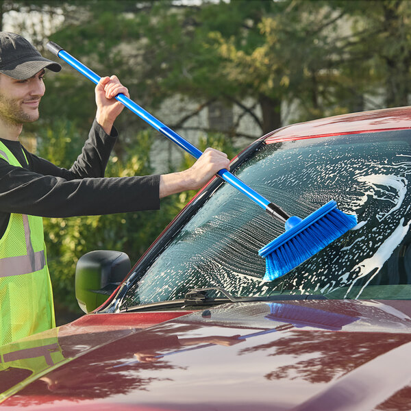 A person cleaning a car with a blue Lavex pole brush.