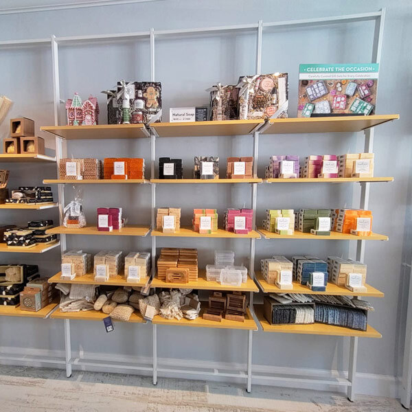 A white Udizine wall-mounted retail clothing display with shelves holding clothing.