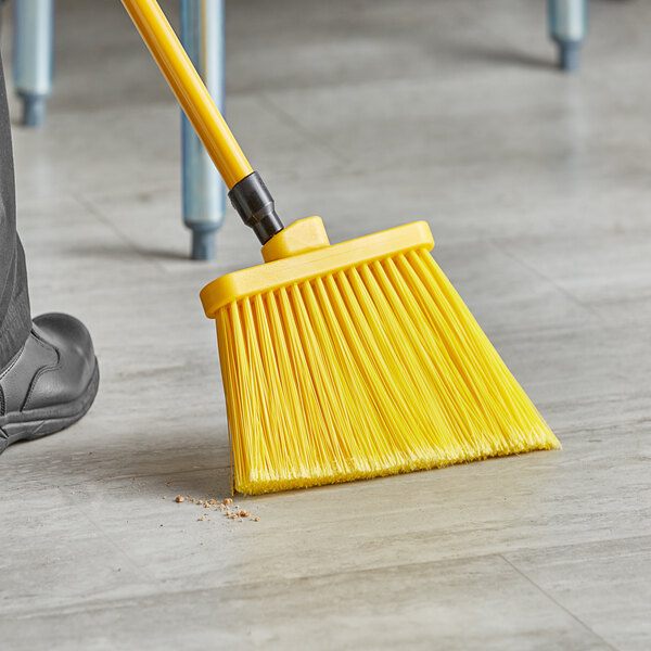 A person sweeping the floor with a yellow Lavex broom.