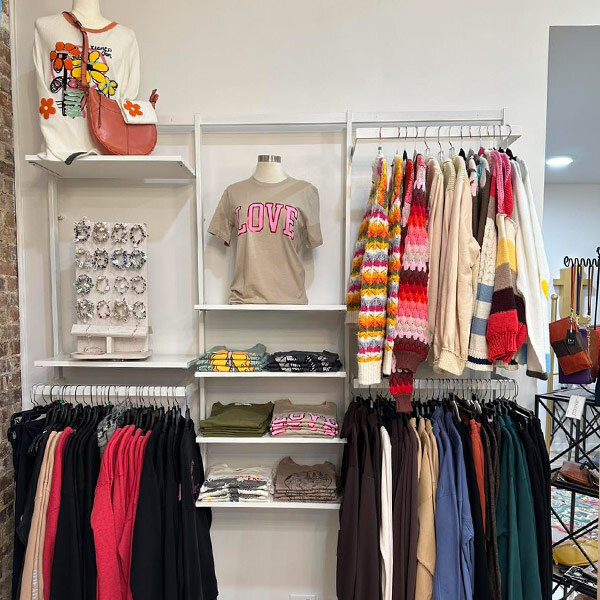 A UDIZINE black wall-mounted retail clothing display with clothes and accessories on it.
