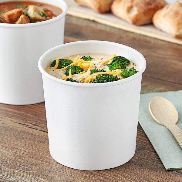 Two white double poly-coated paper food cups of soup with broccoli and cheese.