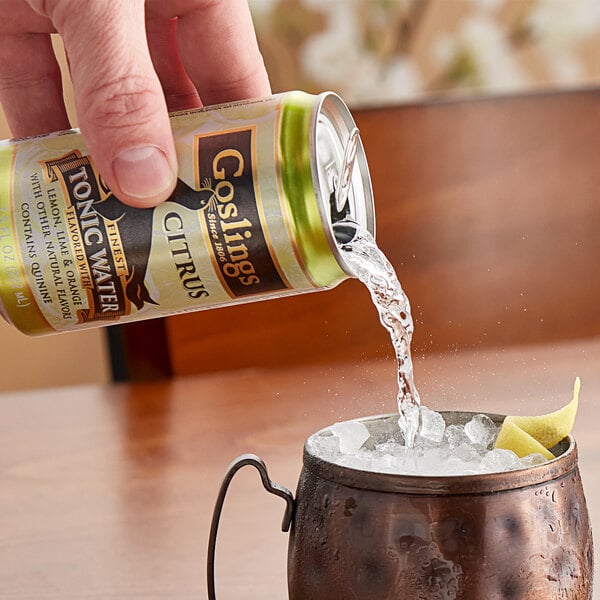 A hand pouring Goslings Citrus Tonic Water into a copper cup with ice.