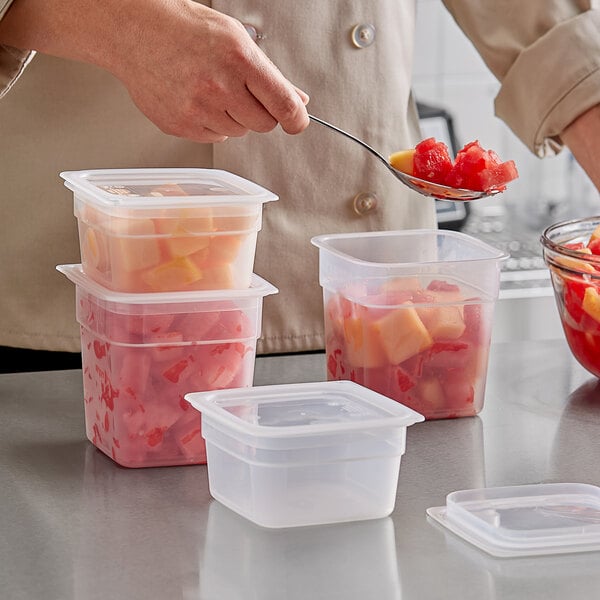 A person using a spoon to scoop fruit from a Cambro FreshPro food storage container with a lid.