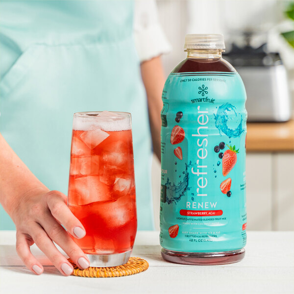 A person holding a glass of Smartfruit Renew Strawberry Acai refresher with ice.