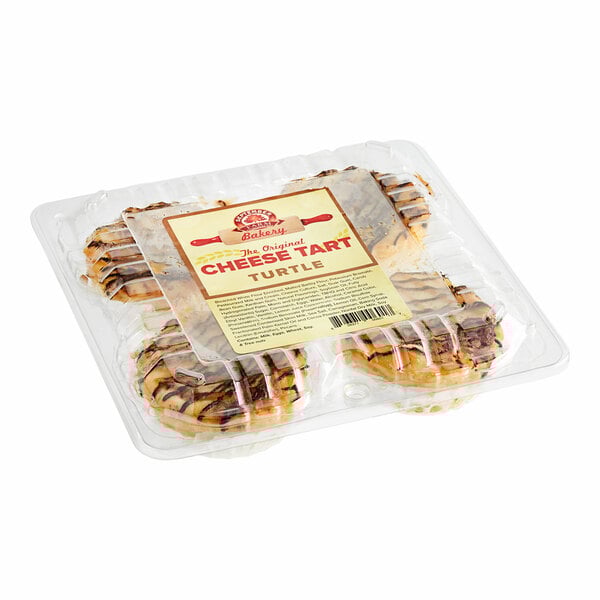 A plastic container of September Farm Turtle Cheese Tarts on a table in a bakery display.