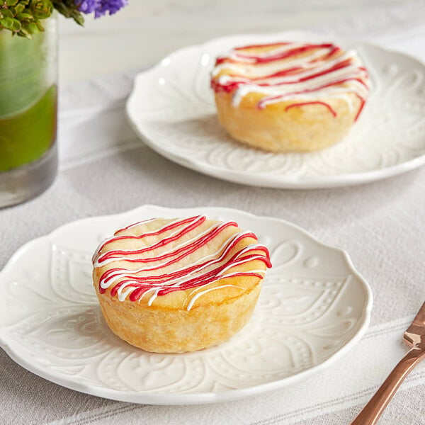 Two September Farm White Chocolate Raspberry Cheese Tarts with white and red frosting on a plate.