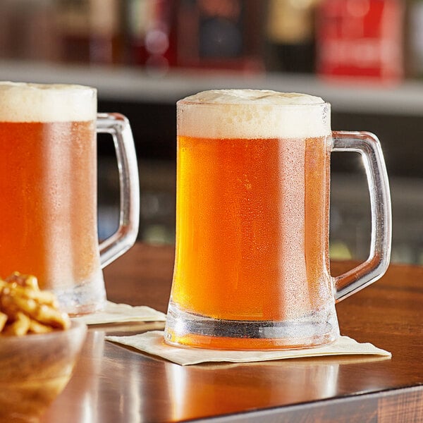 Two Acopa beer mugs filled with beer on a table.