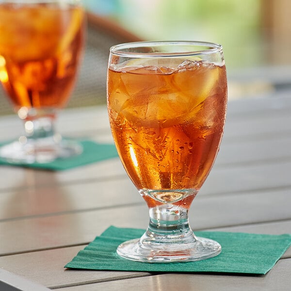 Two Acopa customizable glass goblets of iced tea on a table with a green napkin.