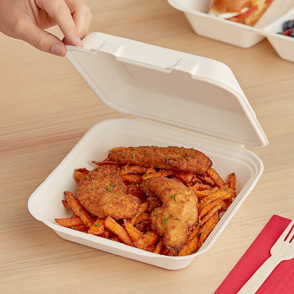 A hand holding a sandwich in a white Dart ProPlanet takeout container.