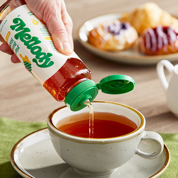 A hand pouring Mellody Plant-Based Vegan Clover Honey into a cup of tea.