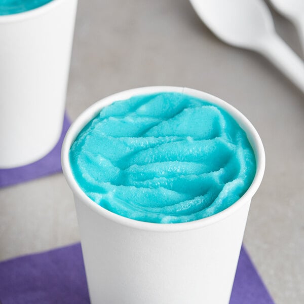 A bowl of blue I. Rice Hawaiian Water Ice on a white surface with a spoon.