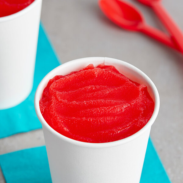 A white cup of red I. Rice cherry limeade water ice with a red spoon.