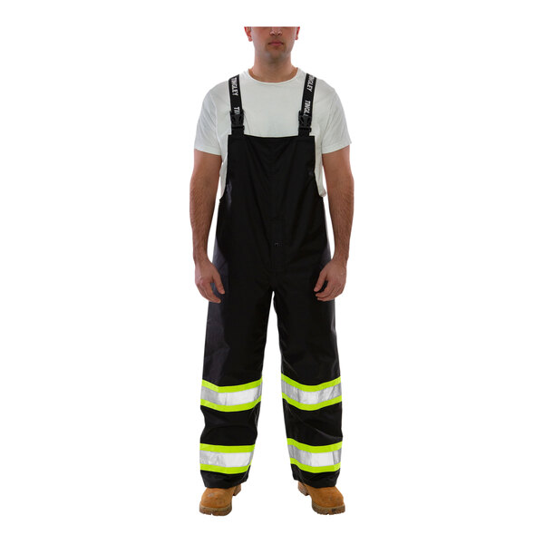 A man wearing Tingley black overalls with reflective stripes.