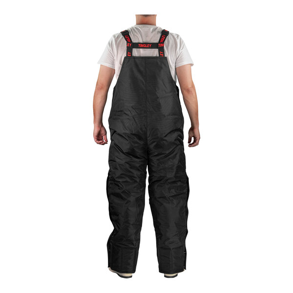 A man wearing black Tingley insulated overalls stands with his back to the camera.