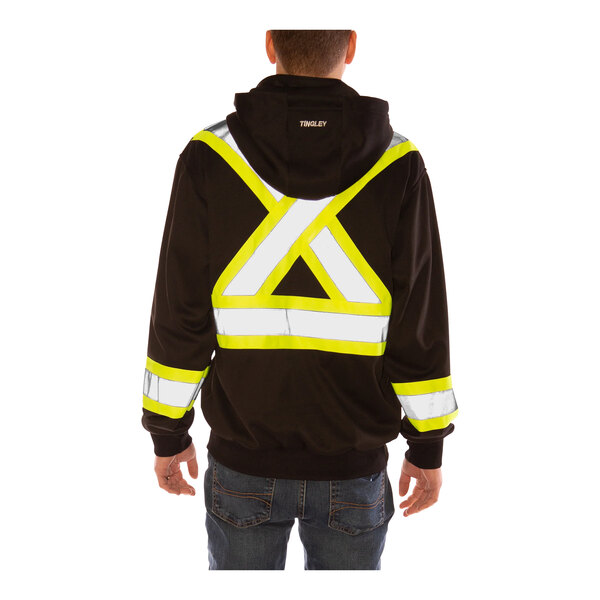 A man wearing a Tingley black zip-up sweatshirt with yellow reflective accents and a detachable hood over a safety vest with reflective tape.